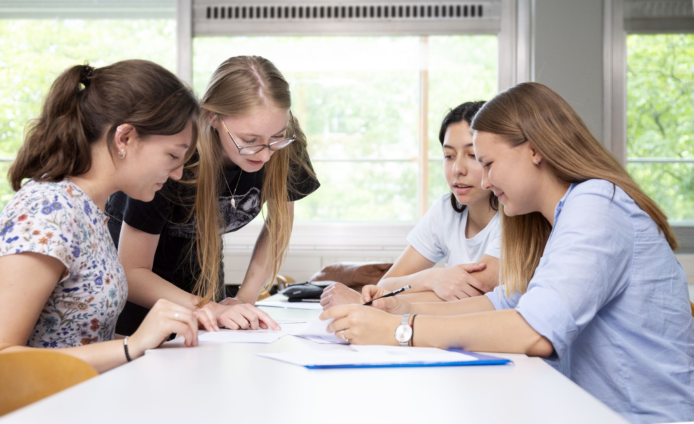 young women grouped around a table, discussing young women grouped around a table, discussing