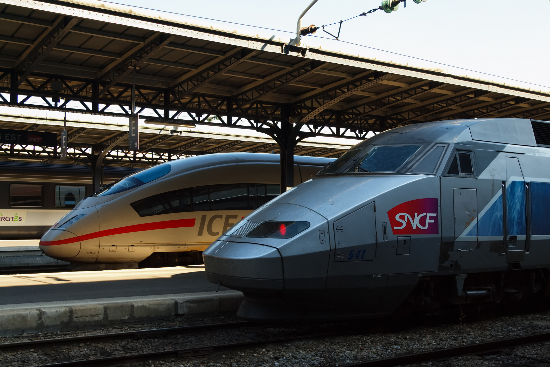 Zwei Züge, ein ICE und ein TGV, stehen nebeneinander im Bahnhof. Ein ICE und ein TGV stehen im Bahnhof nebeneinander.