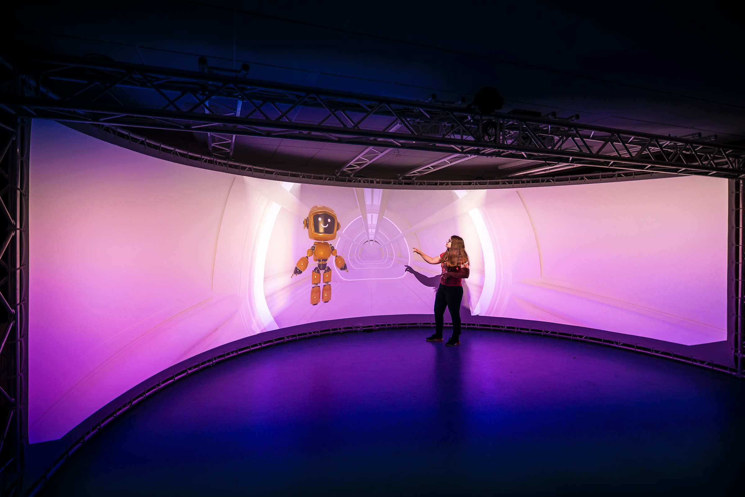 young woman in front of semicircular floor-to-ceiling screen with robot on it young woman in front of semicircular floor-to-ceiling screen with robot on it