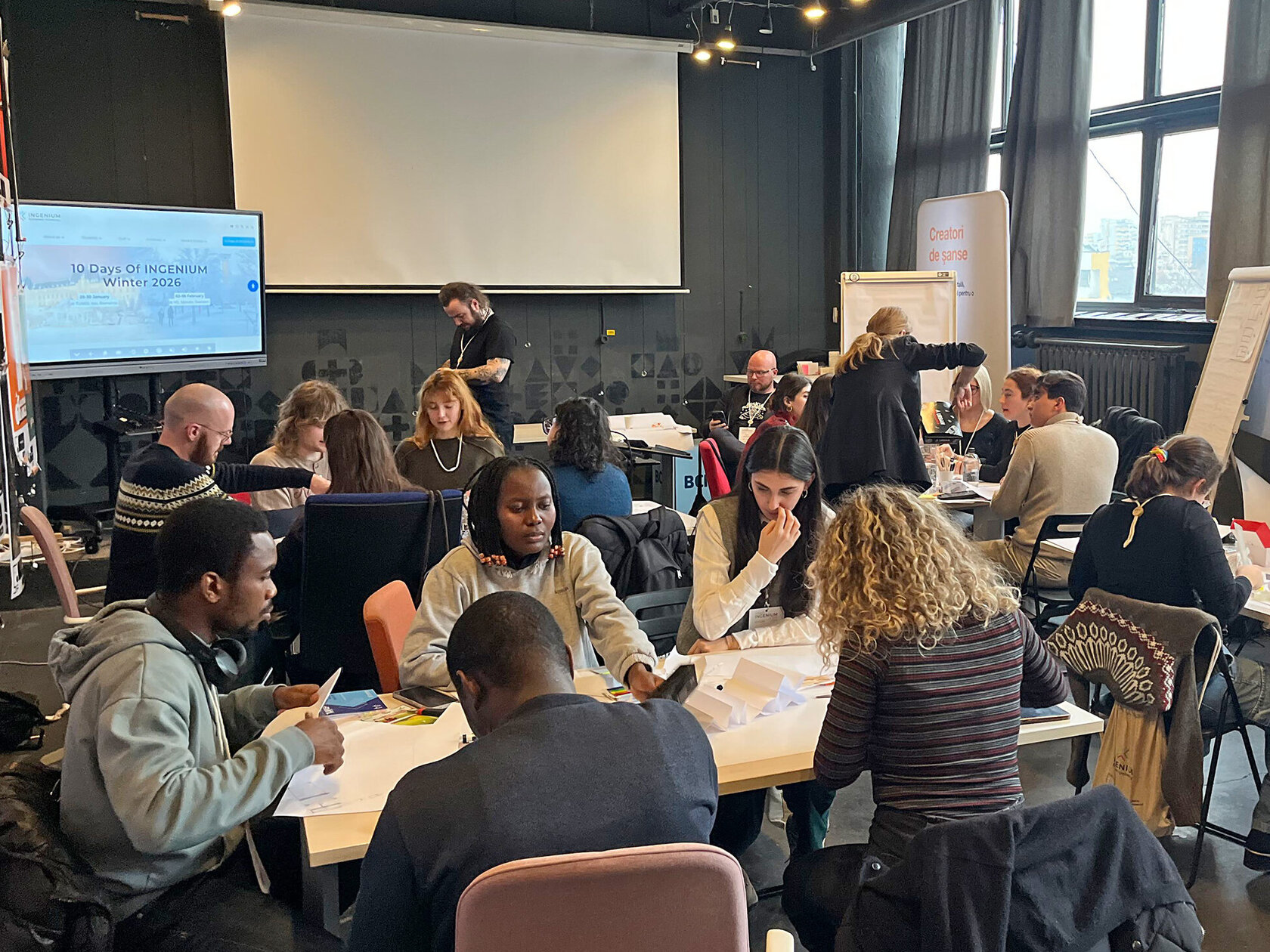 groups of young people working together at tables, with flipcharts dotted around the room