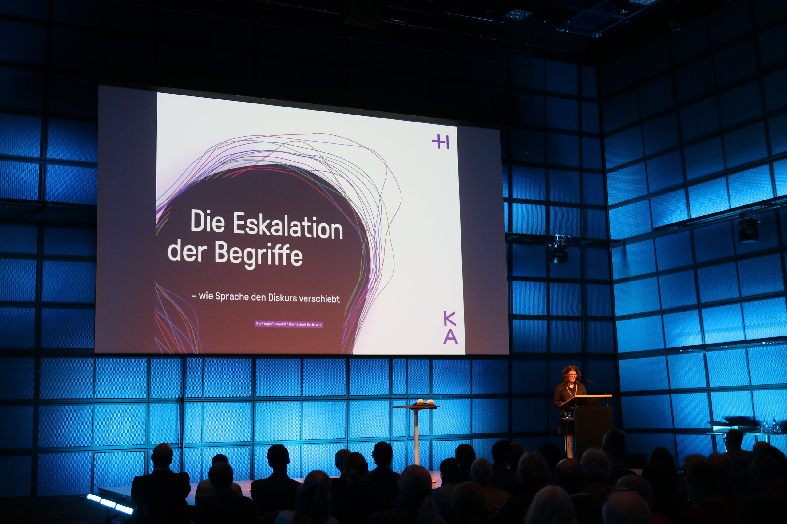 Medientheater des ZKM, Prof. Anja Grunwald auf der Bühne, hinter ihr die Leinwand mit der Titelfolie zu „Eskalation der Begriffe – wie Sprache den Diskurs verschiebt“