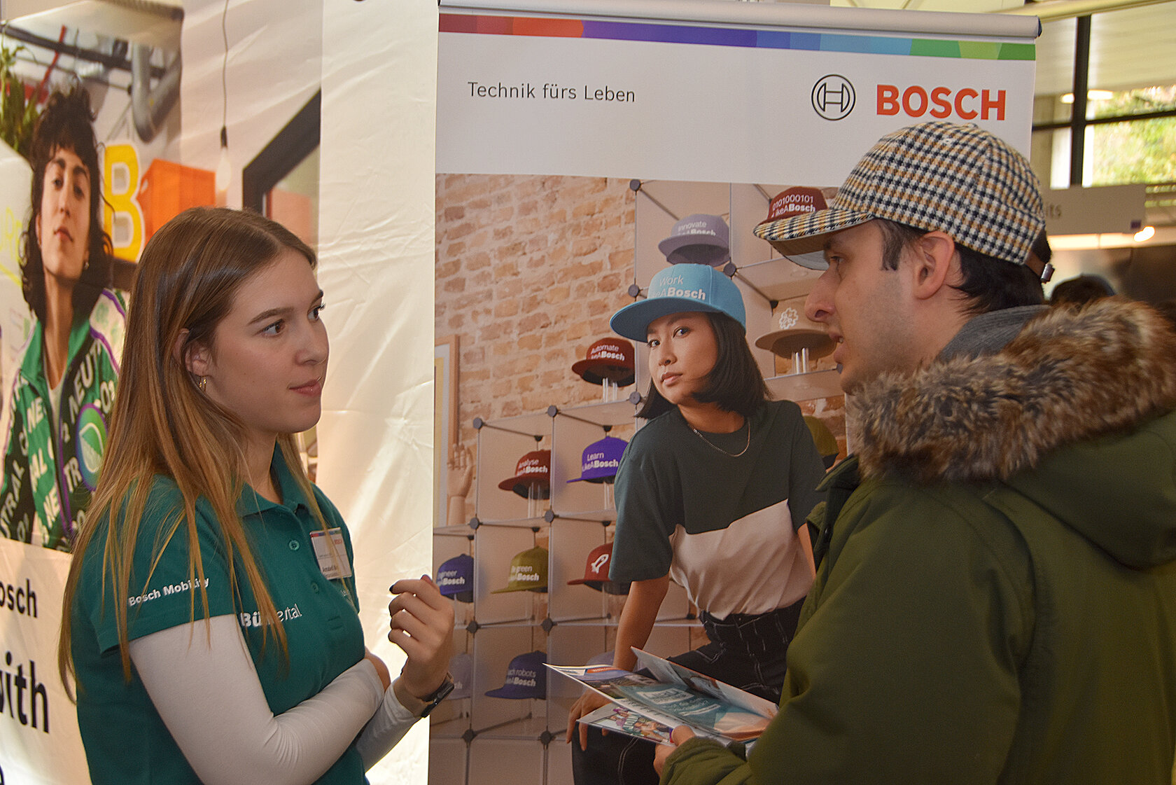 Mitarbeiterin spricht am Messestand der CareerContacts mit einem Studenten, der Informationsmaterial in den Händen hält.