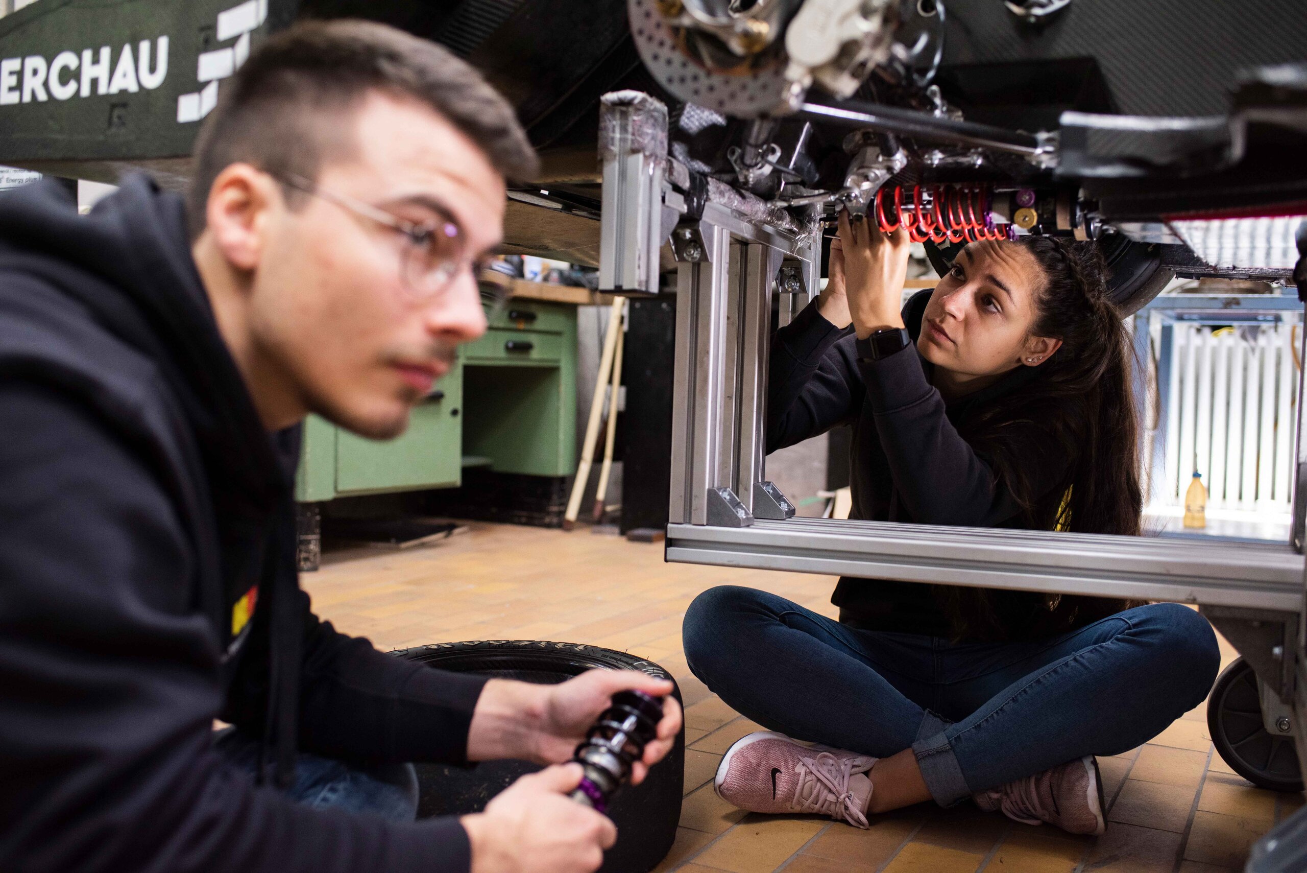 two students sit below a metal frame bearing wires and work on it two students sit below a metal frame bearing wires and work on it