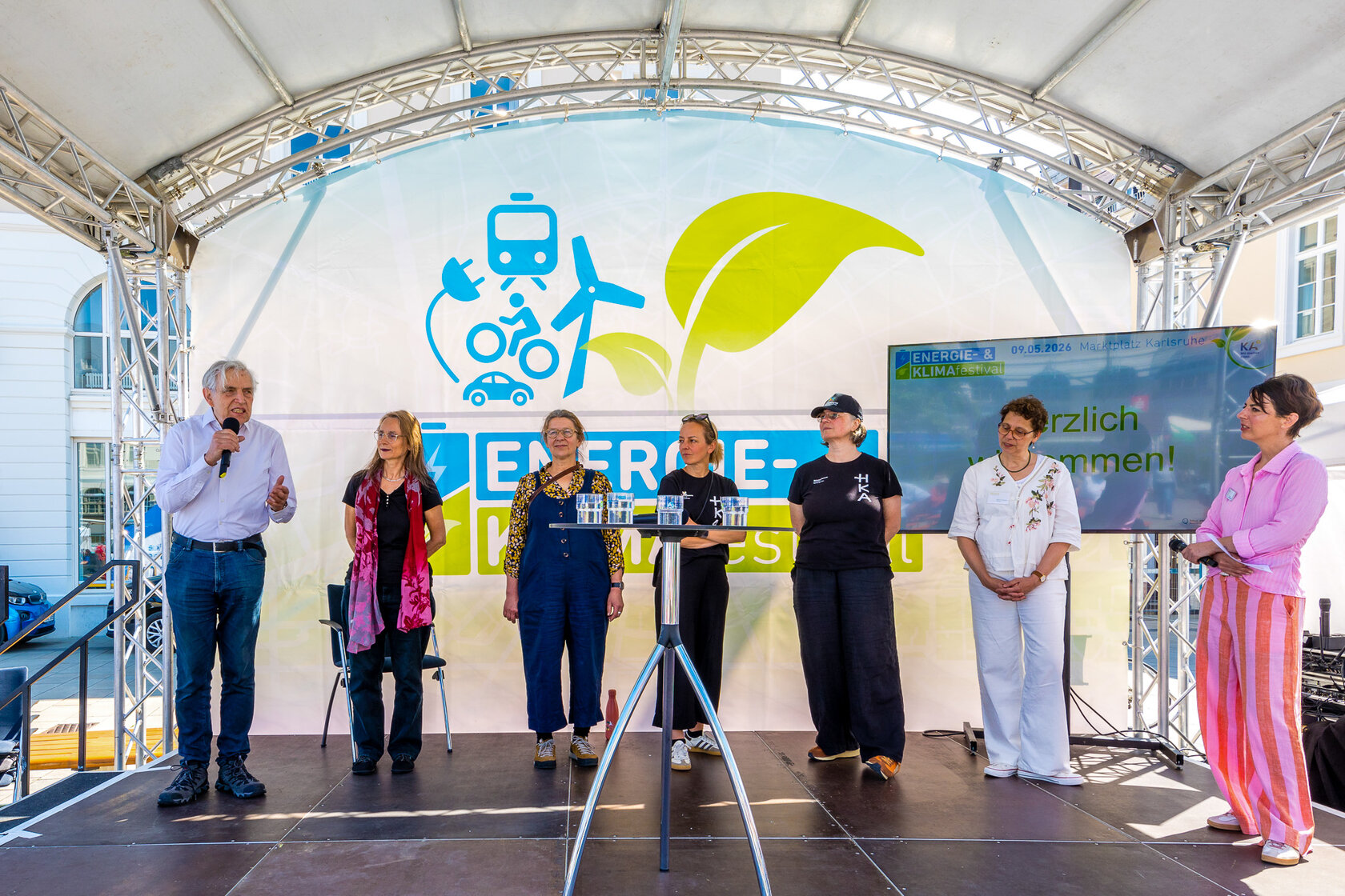 Sechs Personen stehen auf einer Festivalbühne vor dem Banner des Energie- und Klimafestivals, eine Person spricht ins Mikrofon.