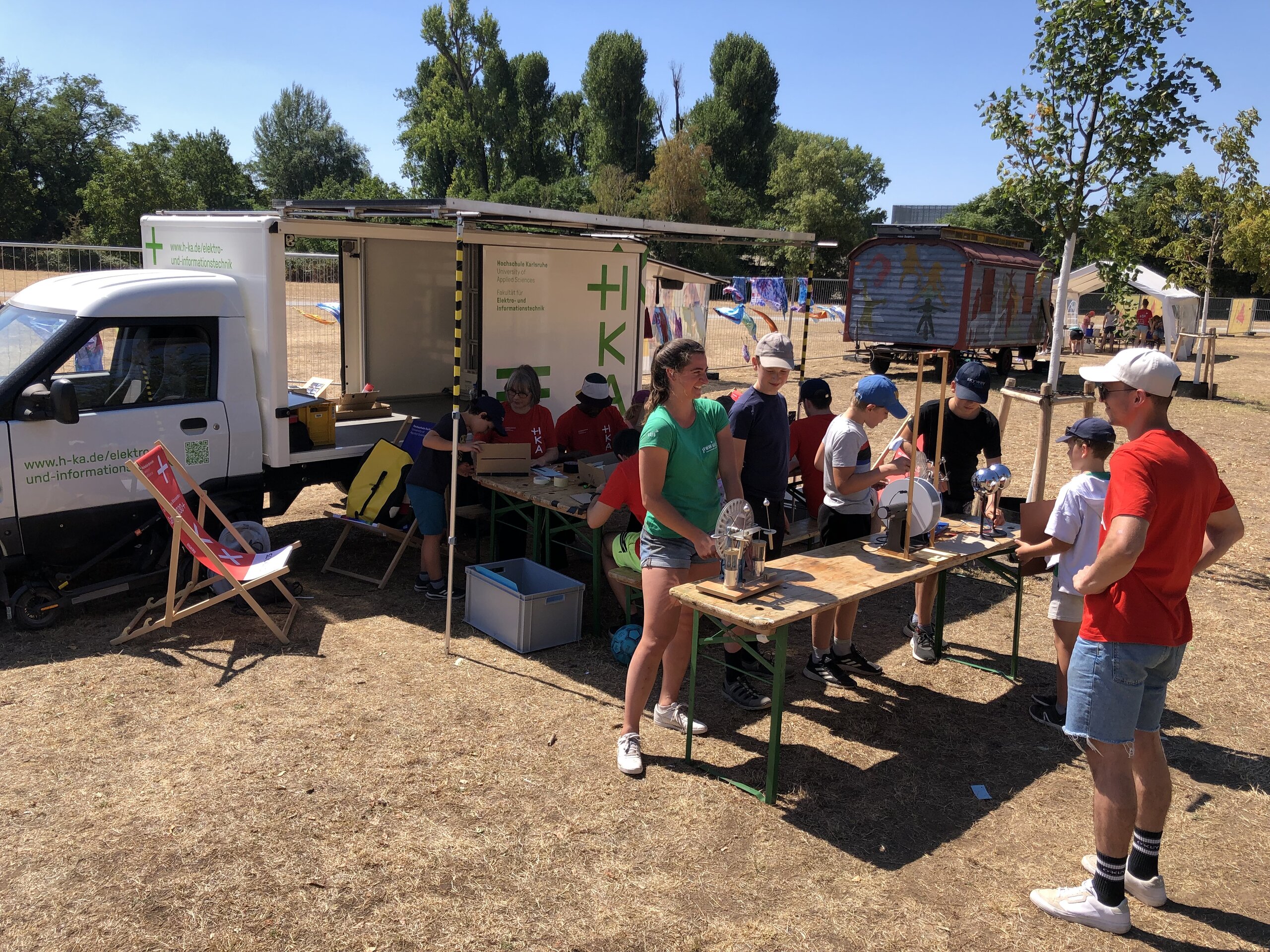 Am Camp der 1000 Möglichkeiten Studierende und Kinder beim Experimentieren mit Elektrotechnik vor dem Solartruck der Fakultät Elektrotechnik.