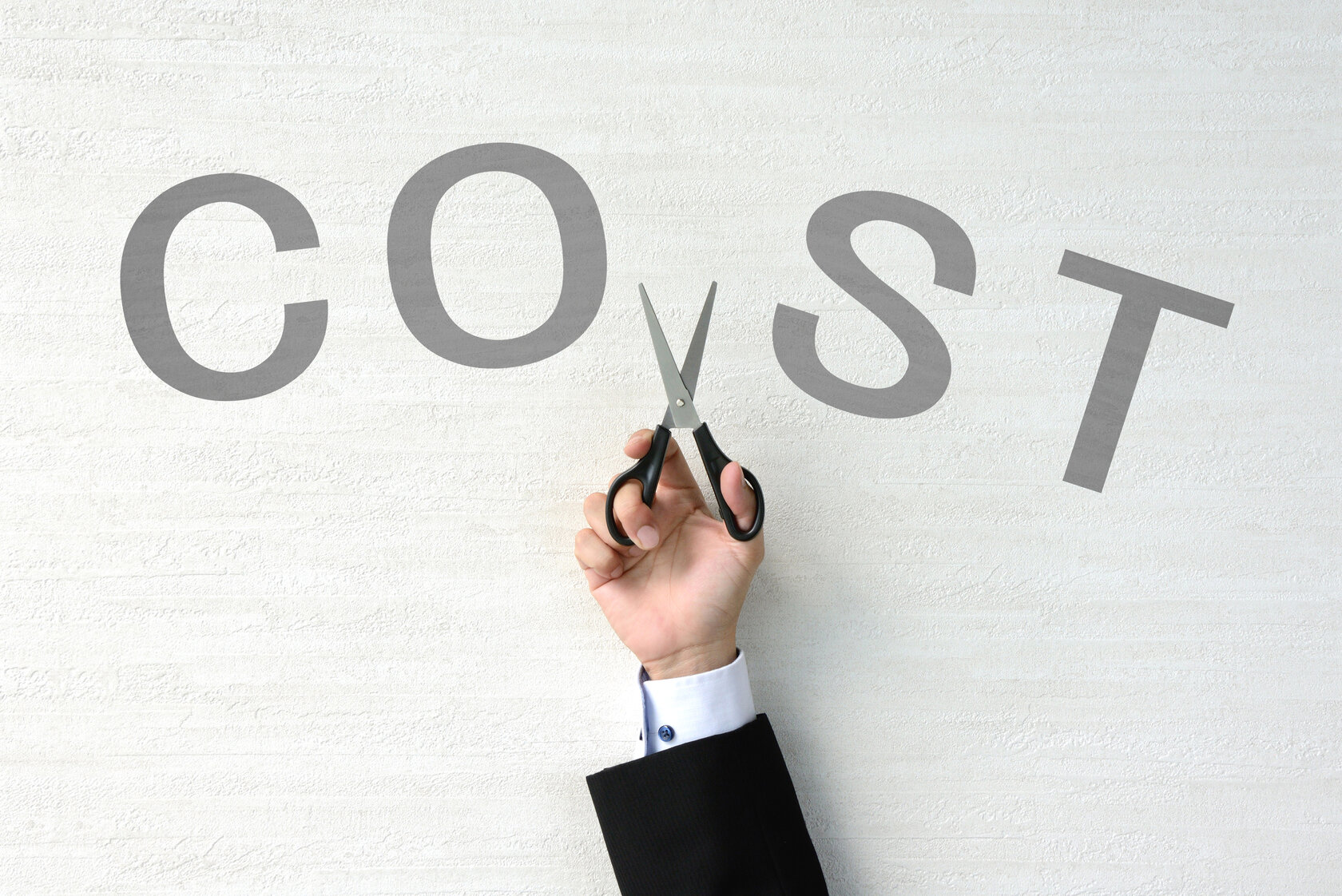 hand cutting the word "cost" in two with scissors hand cutting the word "cost" in two with scissors