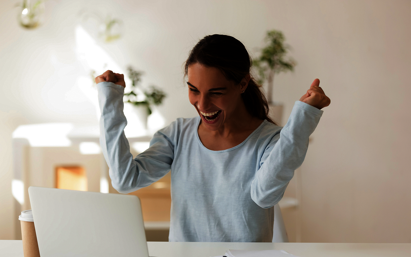 Stipendienberatung positiver Bescheid: junge Frau jubelt beim Blick auf Ihr Notebook