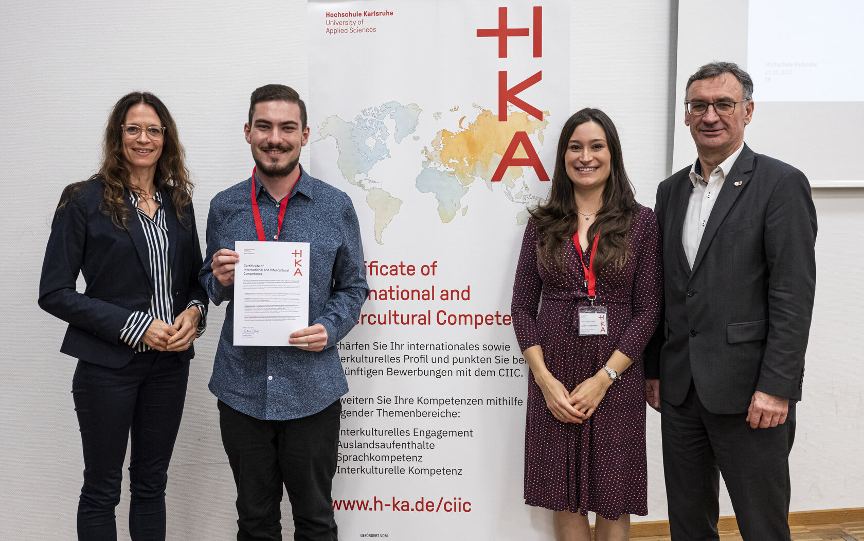 student standing in front of CIIC rollup, presenting his certificate, and surrounded by HKA representatives student standing in front of CIIC rollup, presenting his certificate, and surrounded by HKA representatives