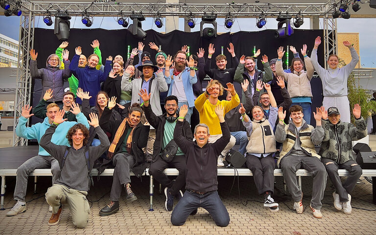 Die 26 Studierenden der Hochschule Karlsruhe und ihre Betreuer stehen auf einer Bühne der Local Conference of Youth 2024 in Berlin und reißen in bester Stimmung die Arme nach oben