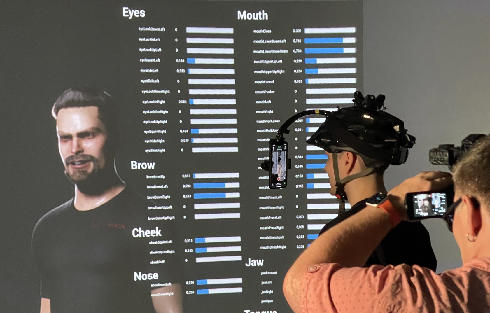 A screen can be seen in the background on which the facial features of the person in the foreground are replicated.