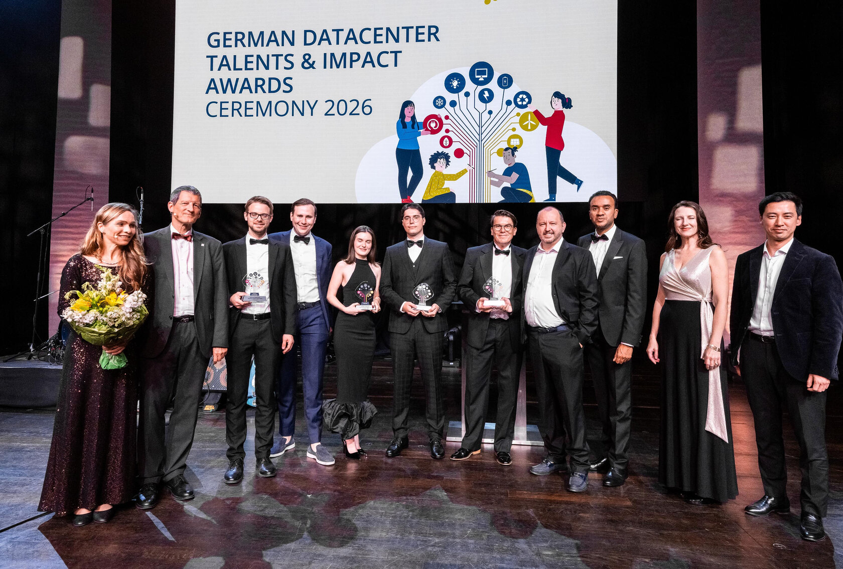 Gruppenfoto der Preisträger*innen und weiterer Beteiligter der German Datacenter Talents & Impact Awards 2026 auf der Bühne. Mehrere Personen halten ihre Auszeichnungen in den Händen.