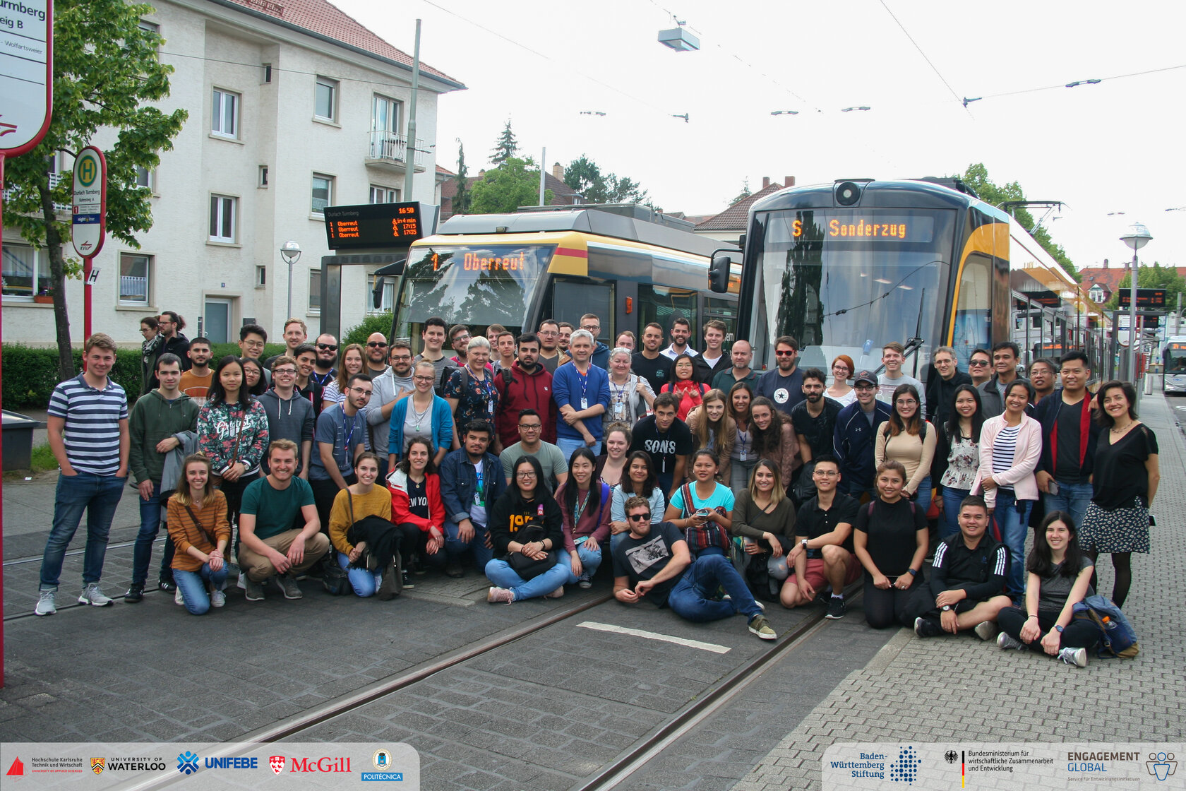 international group of students sitting in front of two trams international group of students sitting in front of two trams