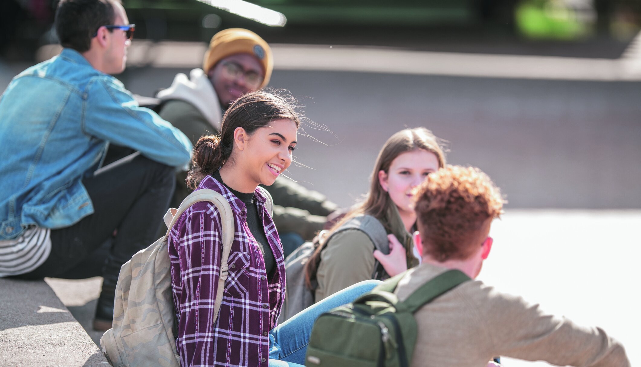 A group of diverse university students enjoy their time on campus together. They are sitting on the steps outside their school and killing time before their next class starts.