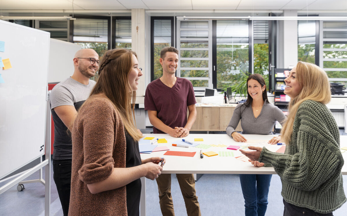 Fünf Menschen unterhalten sich an einem Stehtisch. 