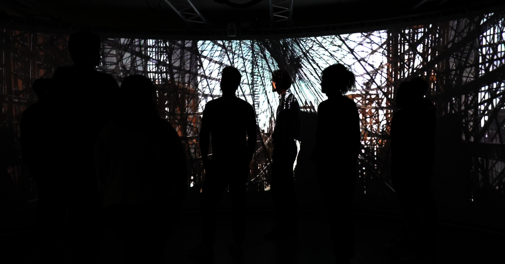 The image shows a group of people in a dark 180-degree projection environment. They are looking at a large-scale projection showing the structure of a historic airship. The scene is kept in muted colors, the people are visible as silhouettes, while the projection is the main focus.